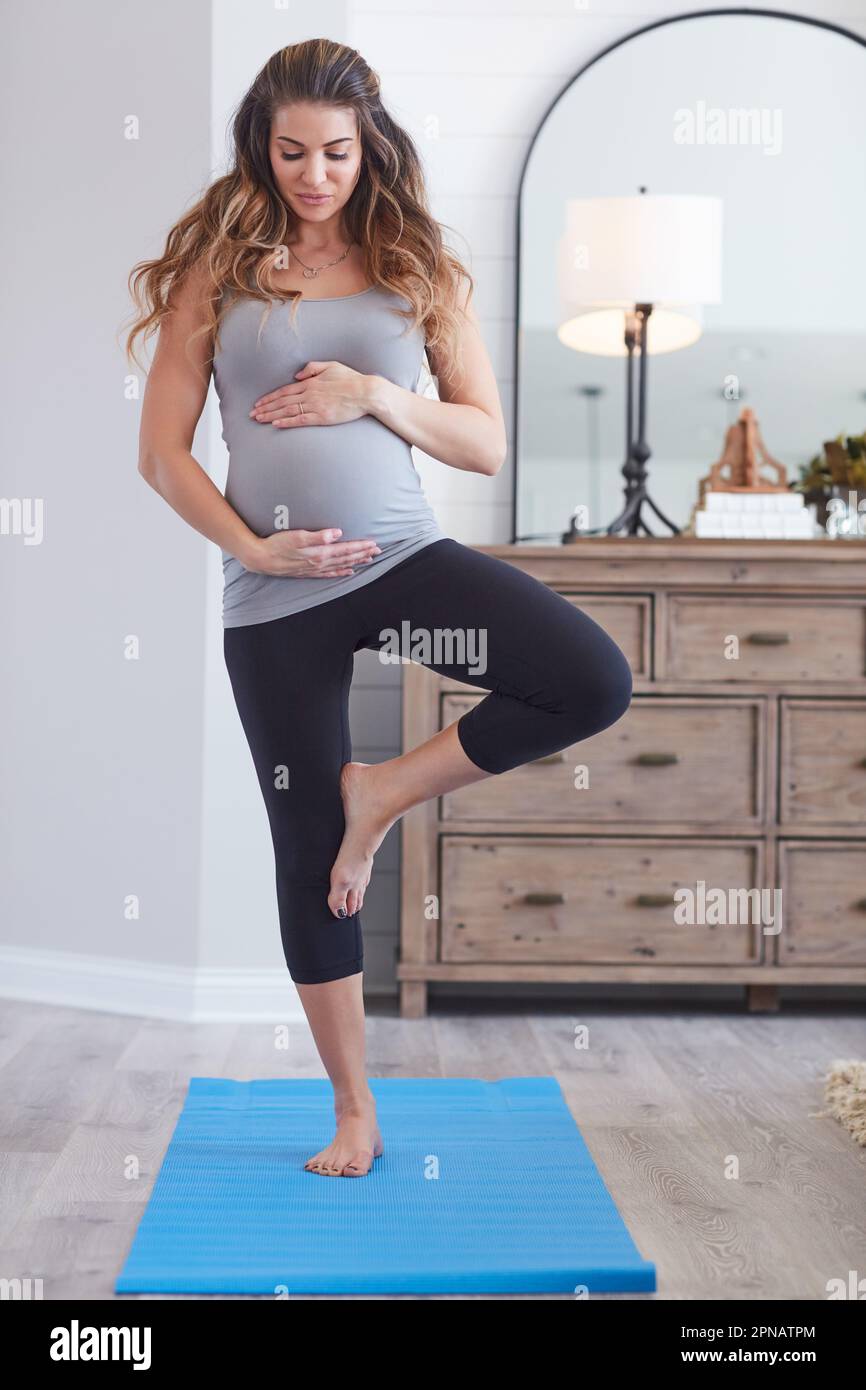 Ci vuole un corpo sano per mantenere una gravidanza sana. una giovane donna incinta che pratica la posa dell'albero durante una procedura di yoga a casa. Foto Stock