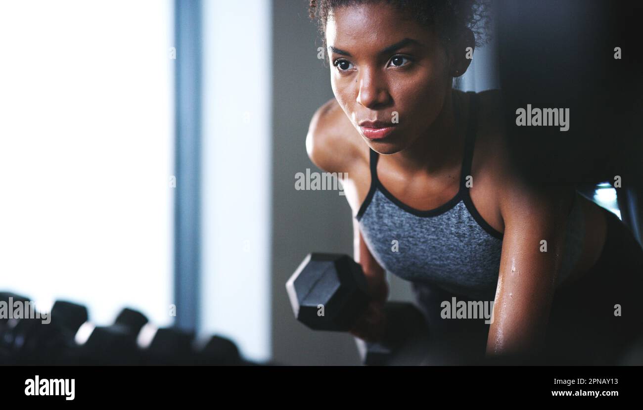 Il suo processo è lento, ma smettere non lo accelera. una giovane donna sportiva che si esercita con un manubrio in palestra. Foto Stock