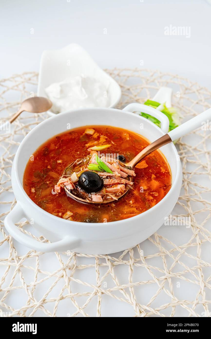 Solyanka di carne. Caldo combinato solyanka. una porzione di zuppa di carne rossa piccante con pomodori, salsicce affumicate e olive con limone su sfondo chiaro. Foto Stock