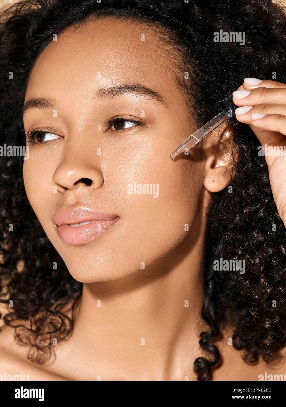 cura della pelle del viso con olio e siero essenziali per il trattamento. Bella donna riccia che applica olio essenziale utilizzando un contagocce per pipette sul viso per idratare S. Foto Stock