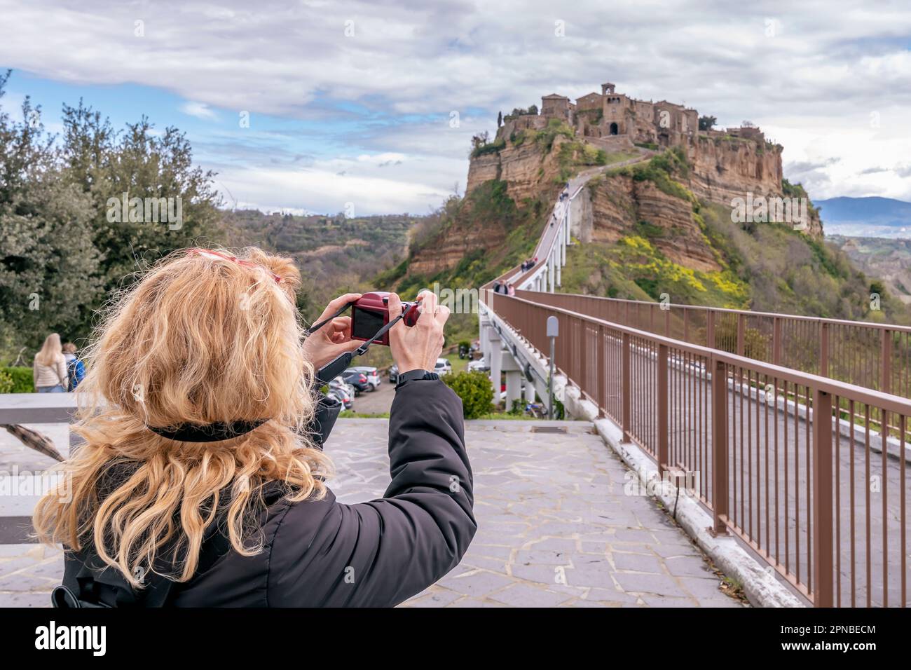 La bionda fotografa l'antico borgo morente chiamato Civita di Bagnoregio, Italia, sotto un cielo drammatico Foto Stock