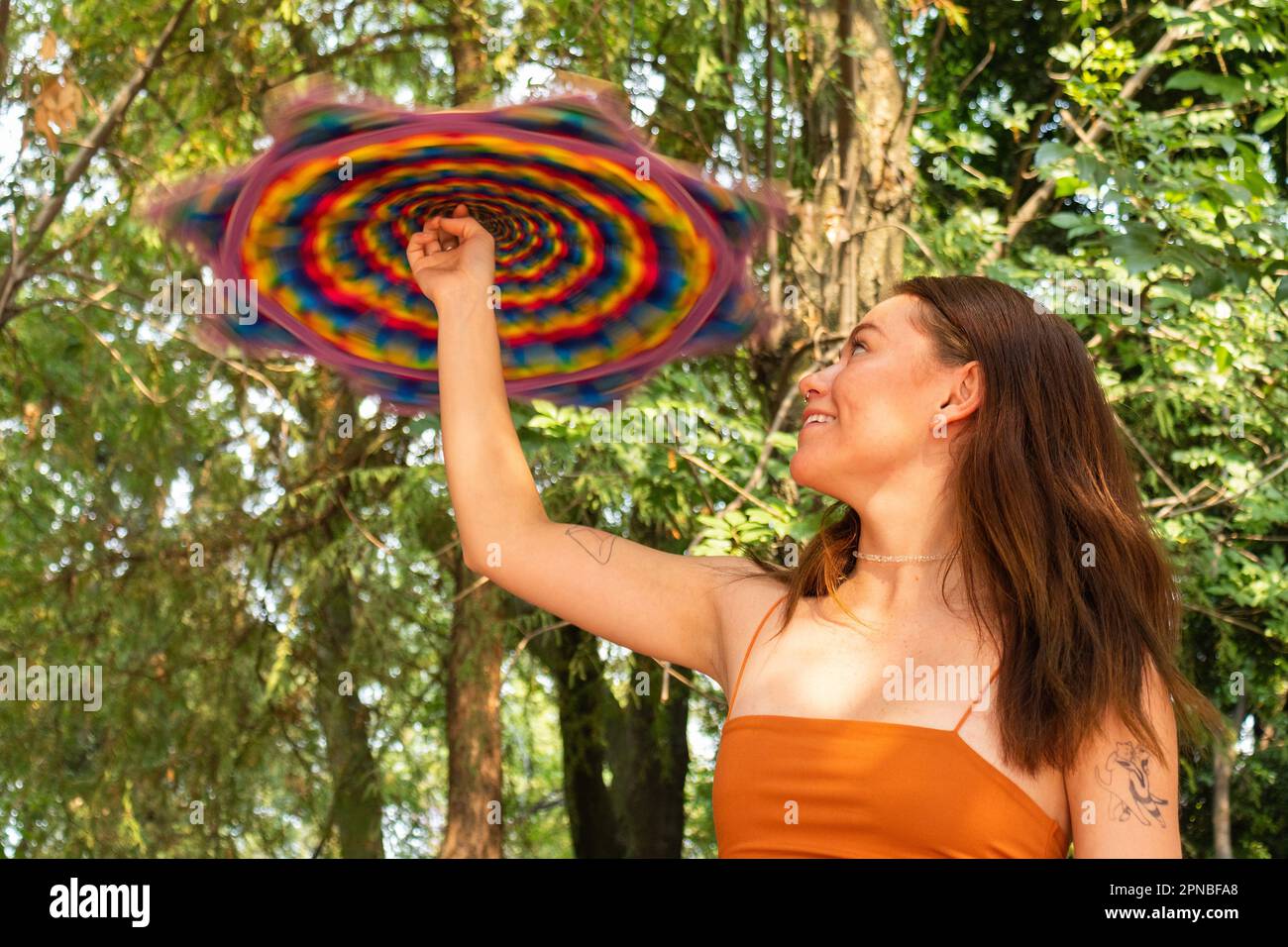 Giovane donna positiva in abito estivo arancione sorridente e lancio Dapo mentre si gioca a giocoleria Foto Stock