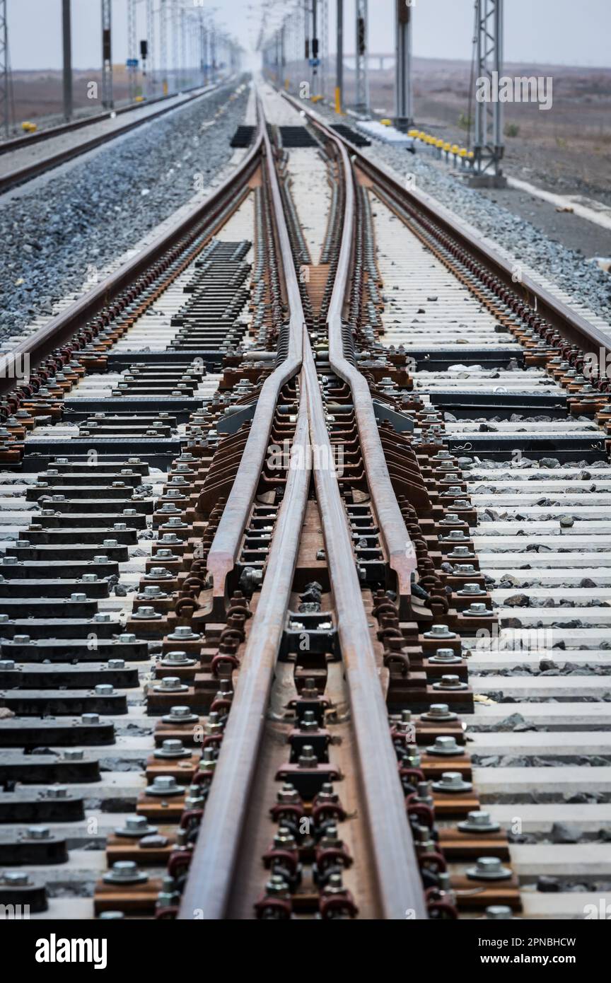 Lunghe rotaie rettilinee per treni che corrono con congiunzione tra rotaie metalliche su terreno roccioso durante il giorno Foto Stock
