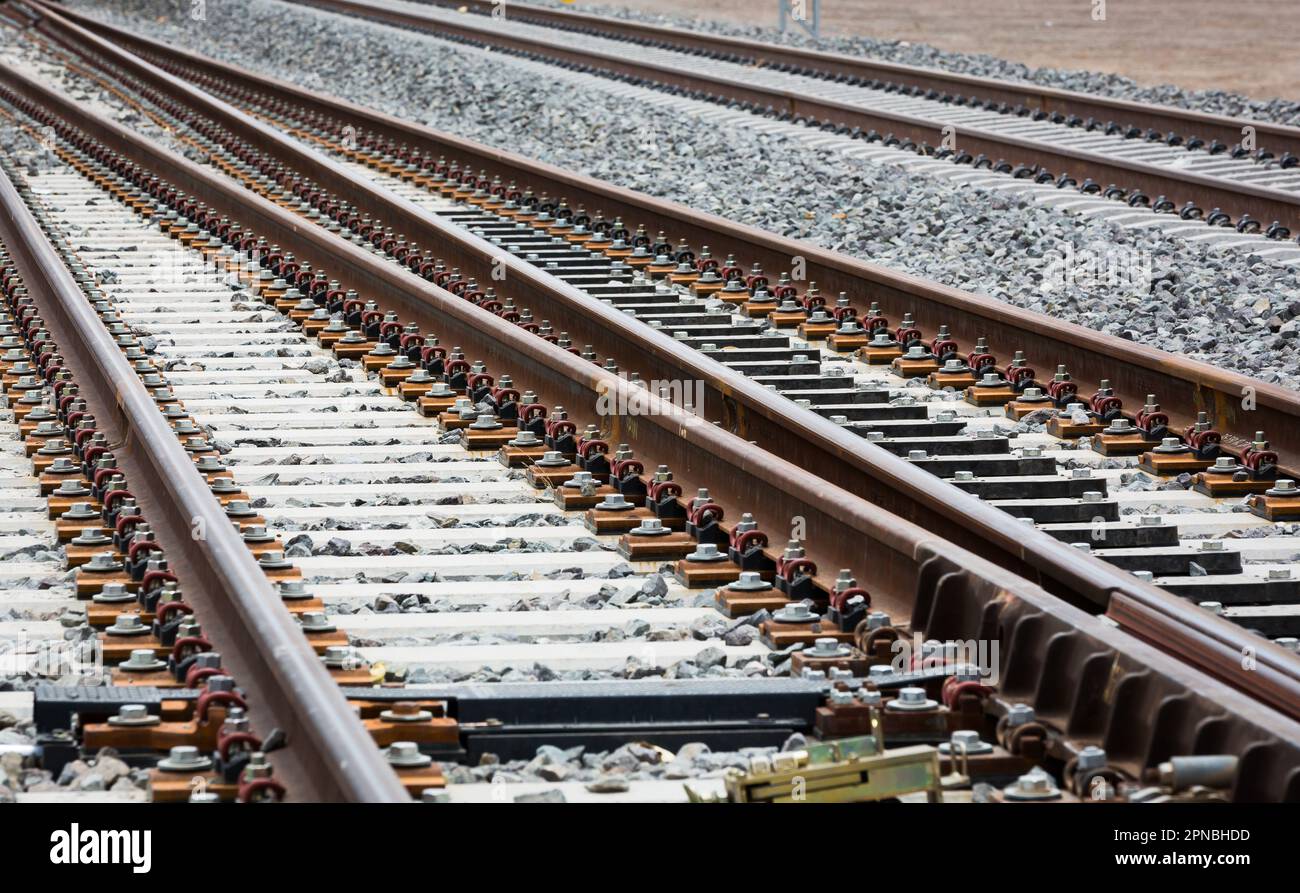 Lunghe rotaie rettilinee per treni che corrono con congiunzione tra rotaie metalliche su terreno roccioso durante il giorno Foto Stock