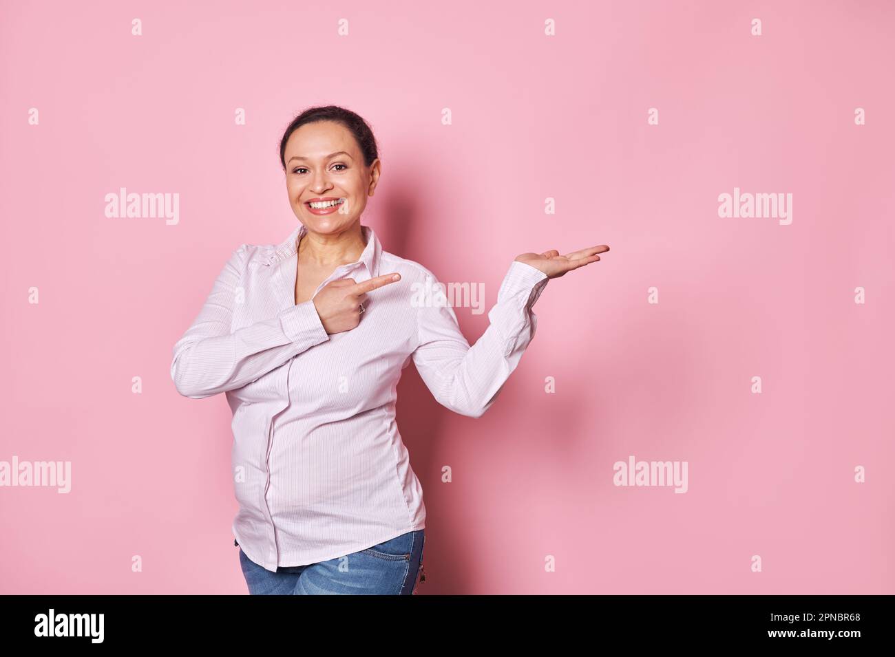 Una donna incinta sorride davanti alla fotocamera, punta il dito indice sullo spazio delle copie sul palmo della mano. Ginecologia maternità Pegnancy Foto Stock