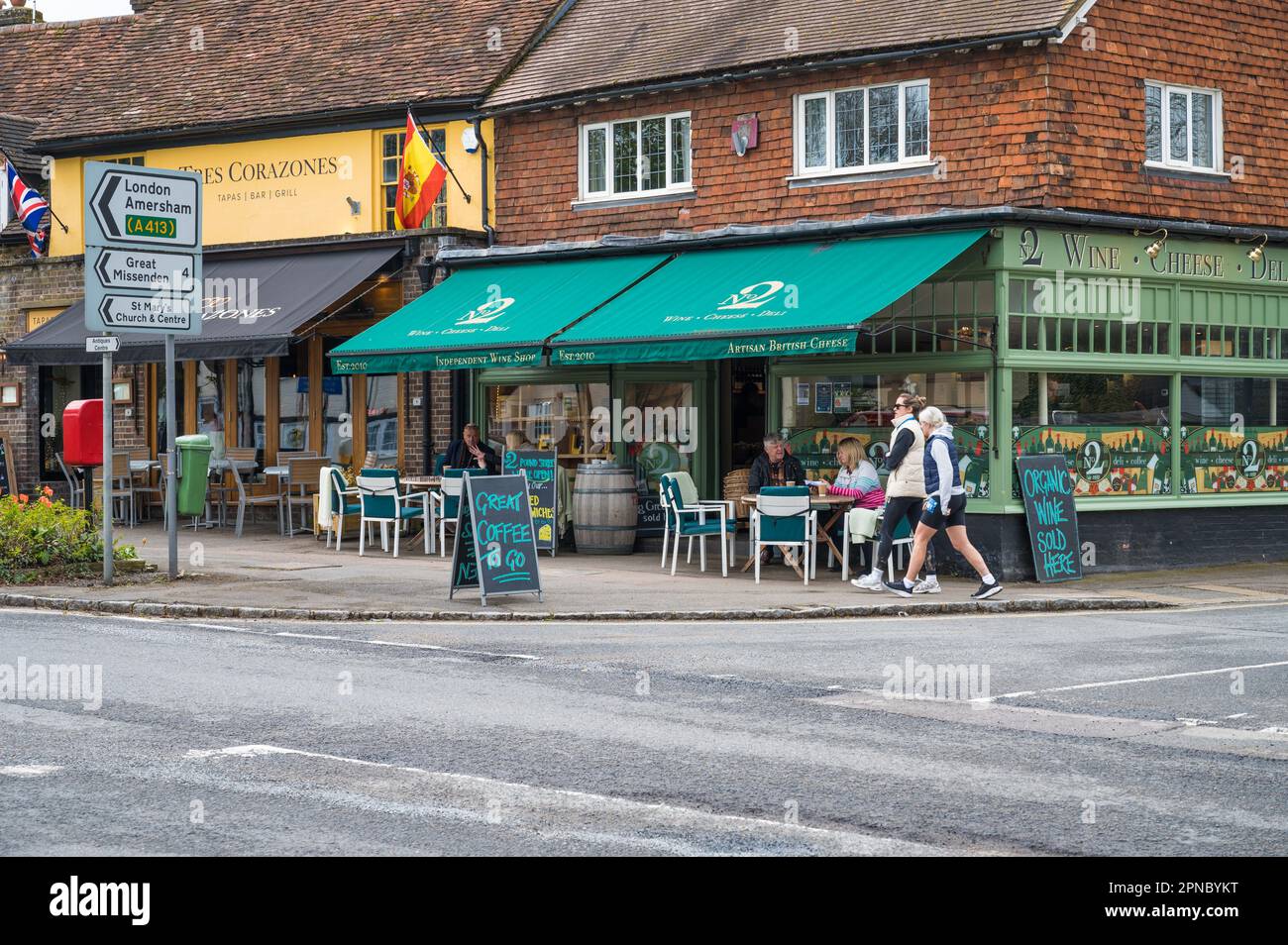 Le persone sedute ai tavoli del marciapiede possono gustare dei rinfreschi al NO2 di Pound Street, un negozio di formaggi e vini e un negozio di specialità gastronomiche. Wendover, Buckinghamshire, Inghilterra Foto Stock