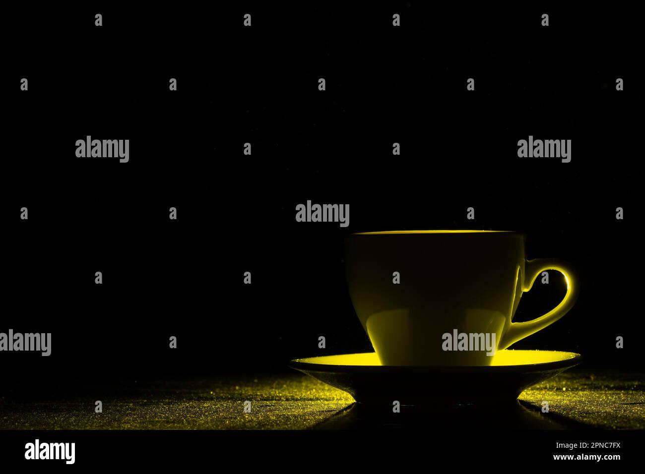 Una tazza con una bevanda calda illuminata da luce gialla su sfondo nero, silhouette, spazio copia, creativo. Caffè mattutino Foto Stock