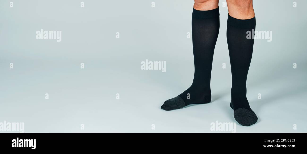 un uomo, in piedi su uno sfondo bianco sporco, indossa un paio di calze nere a compressione, in un formato panoramico da utilizzare come banner web o intestazione Foto Stock