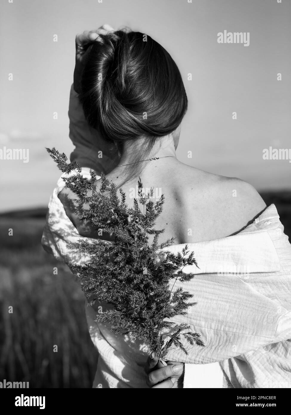 Una vista posteriore di una donna in una camicia bianca che tiene un bouquet di fiori viola Foto Stock