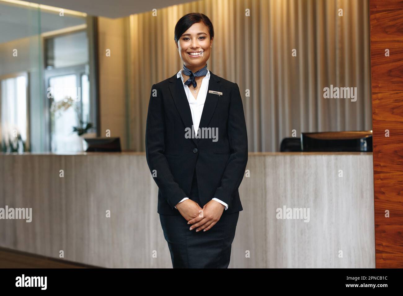 Giovane addetta al ricevimento asiatica che si sente fiduciosa nel suo abbigliamento formale, sorridendo e guardando la macchina fotografica. Dipendente dell'ospitalità femminile che lavora come concierge Foto Stock