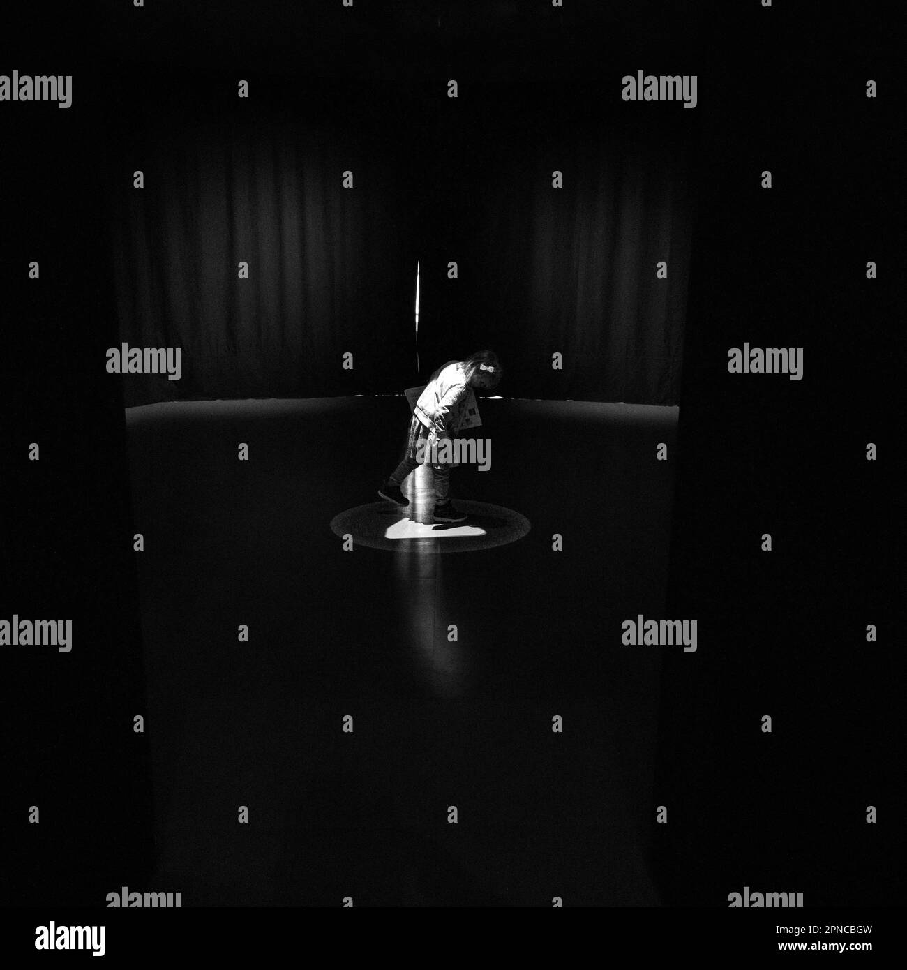 Immagine in scala di grigi di una persona in piedi in una stanza buia, illuminata da una singola sorgente luminosa. Foto Stock