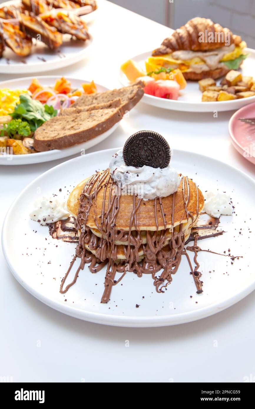 Gocce di cioccolato su torta tagliata in padella con altri piatti per la colazione sullo sfondo. Foto Stock