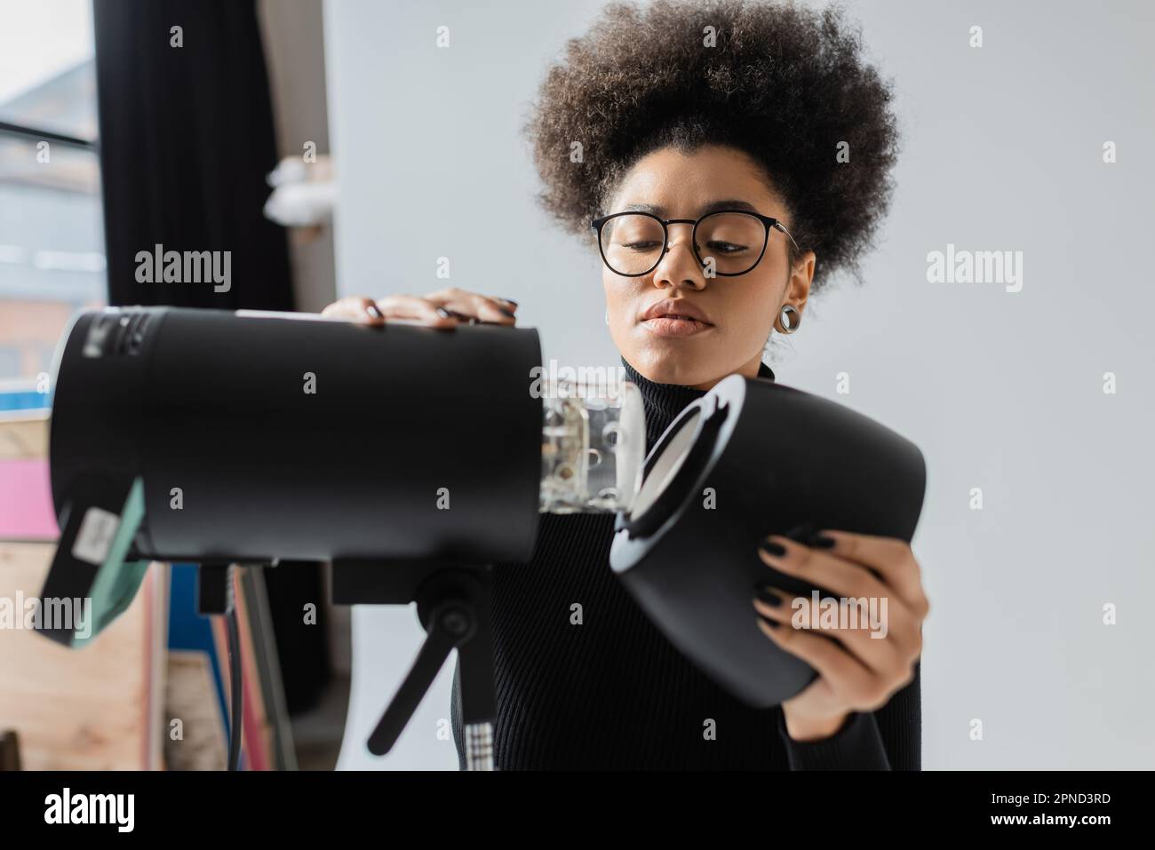 african american content maker in occhiali montaggio strobe riflettori in studio fotografico, immagine stock Foto Stock