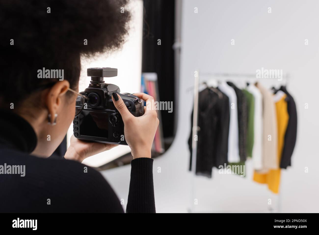 creatore di contenuti afroamericano fotografare la collezione sfocata di vestiti in studio fotografico, immagine di scorta Foto Stock