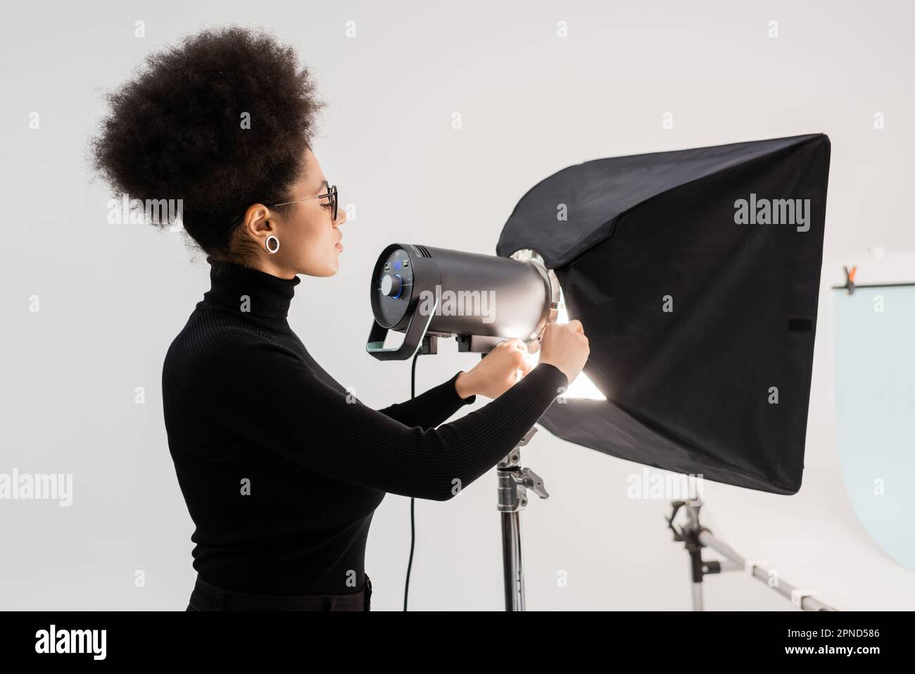 vista laterale del content maker afro-americano che monta riflettori e softbox in studio fotografico, immagine stock Foto Stock