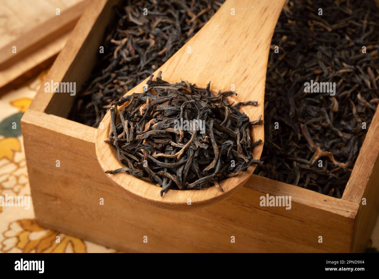 Assam indiano nero Harmutty foglie di tè secco su un cucchiaio di legno in una scatola da tè primo piano Foto Stock