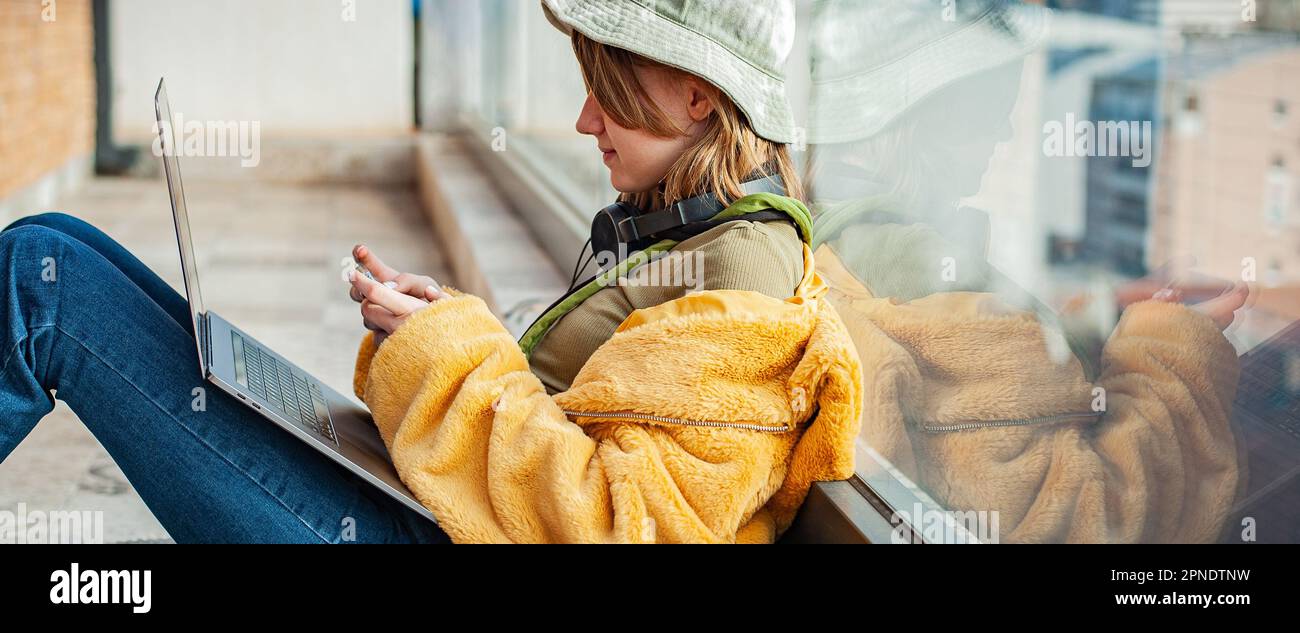 Ragazza adolescente Hippster seduta con computer portatile sulla terrazza con vista sulla città. Giovane donna felice che usa il laptop, lo shopping o che lavora online da casa Foto Stock