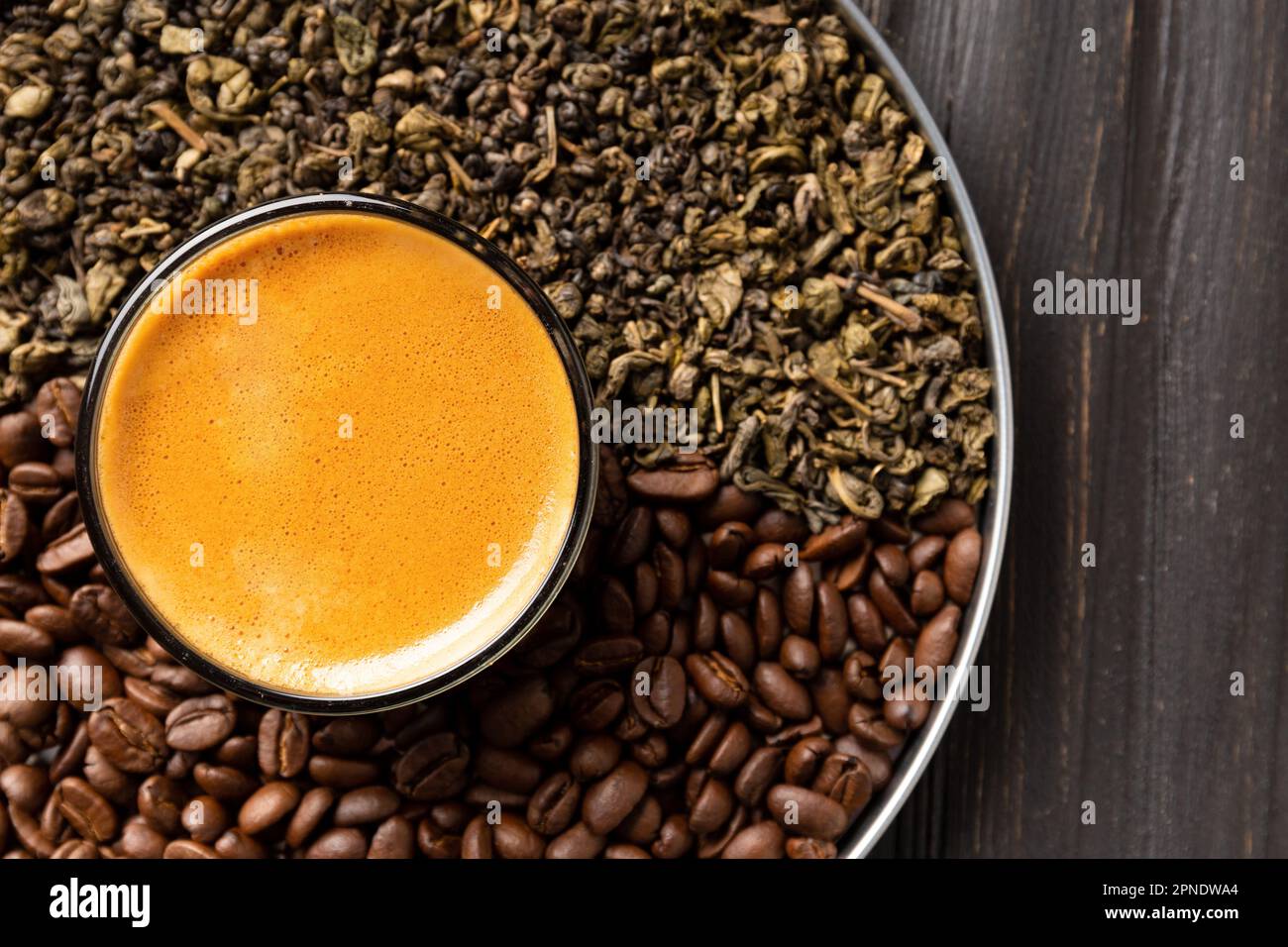 Composizione di foglie di tè verde secco, chicchi di caffè tostati in una scatola rotonda e caffè in una tazza su uno sfondo di legno scuro vista dall'alto. Foto Stock