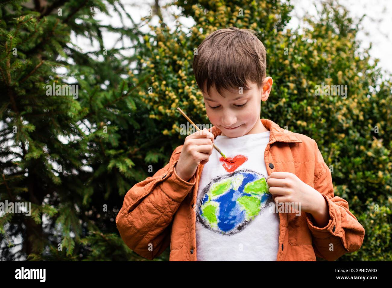Concetto di stile di vita sostenibile. Scolaro che disegna il globo della terra sulla t-shirt. Energia verde, ESG, risorse rinnovabili, tutela dell'ambiente, protezione del pianeta Foto Stock