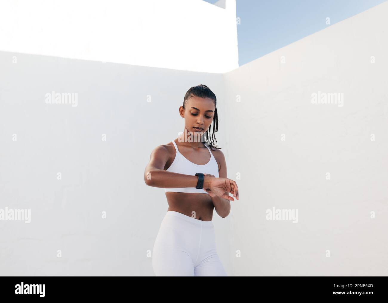 Giovane donna snella che controlla la frequenza cardiaca nello studio bianco all'aperto. Fitness femminile guardando lo smartwatch controllo polso. Foto Stock