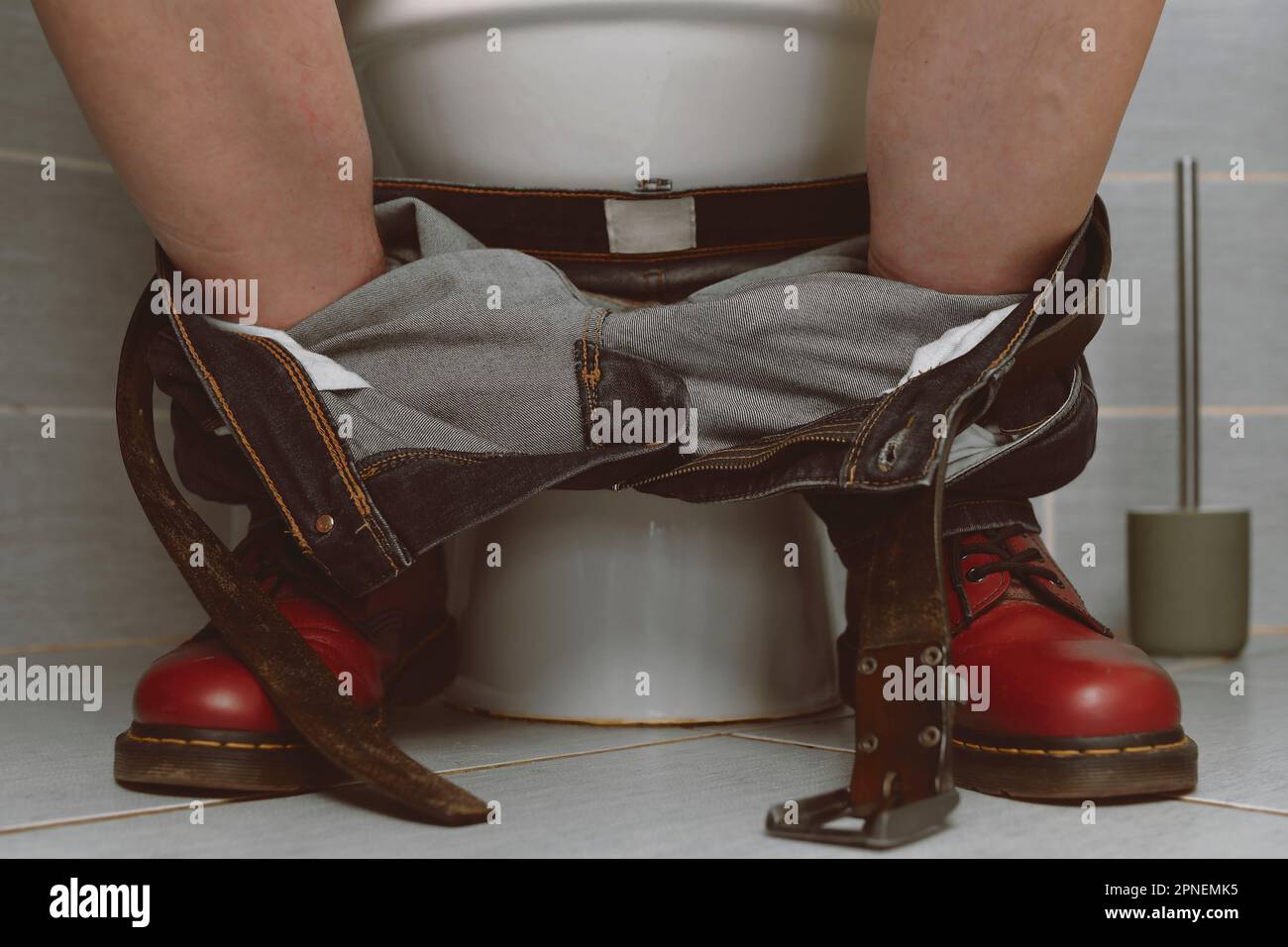 Un uomo seduto sul gabinetto. Un concetto del 1980s. Scarpe e jeans punk rossi Foto Stock