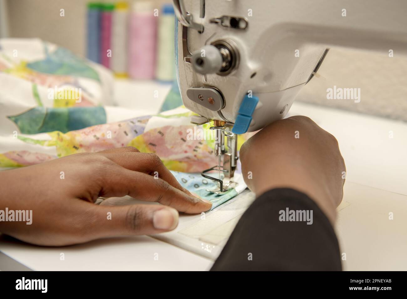 Mani di una donna dai capelli scuri che utilizza una macchina da cucire industriale Foto Stock