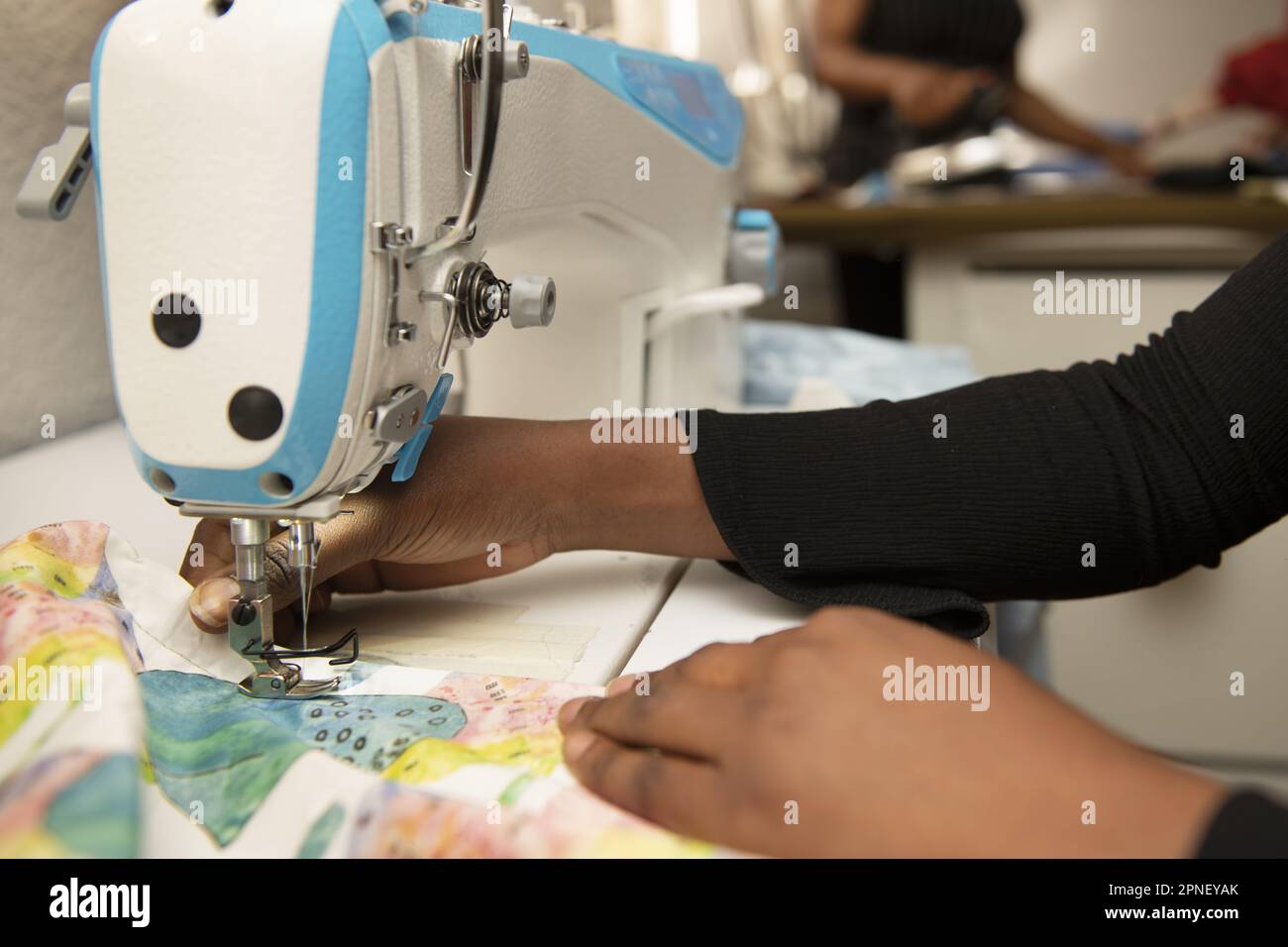 Mani di una donna dai capelli scuri che utilizza una macchina da cucire industriale in un laboratorio di cucito Foto Stock