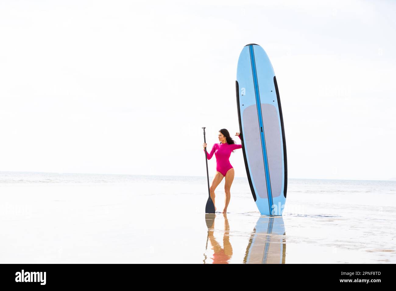 Donna in piedi accanto al paddleboard sulla spiaggia di sabbia Foto Stock