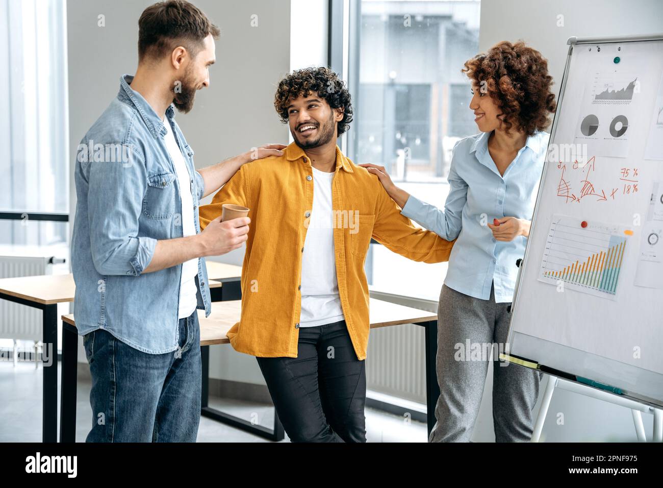 Gruppo motivato di colleghi multirazziali, team creativo di top manager, stare in un ufficio moderno vicino a una lavagna bianca, comunicare, sono soddisfatti dei risultati del lavoro, sorriso Foto Stock