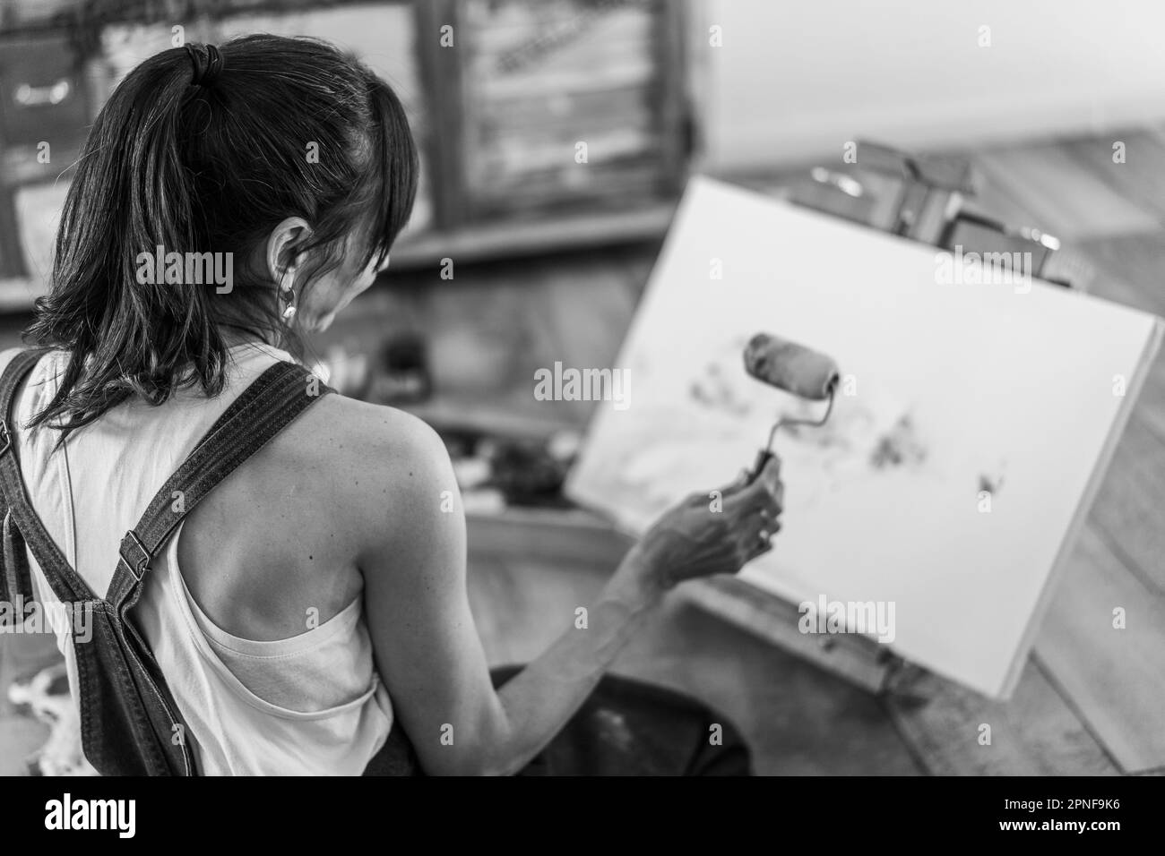 Donna artista pittura su una tela sul pavimento nel suo studio d'arte. Bianco e nero. Foto Stock
