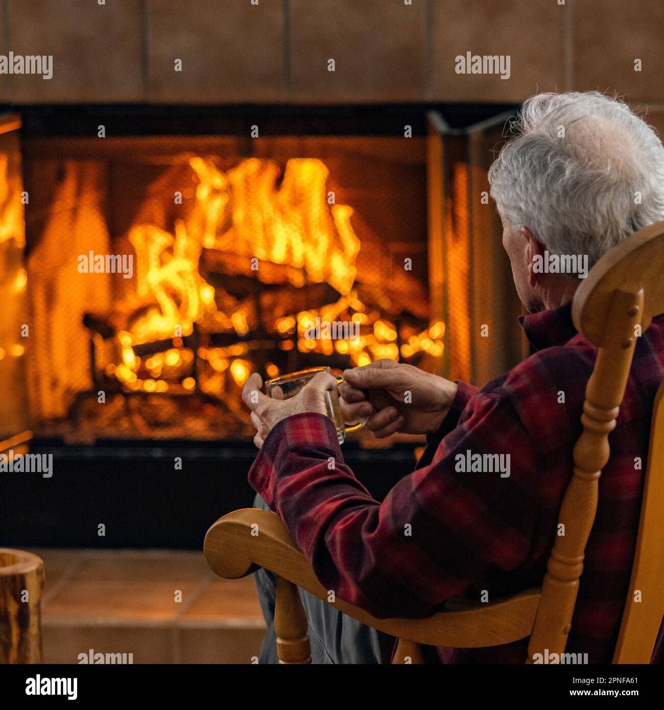 Uomo anziano che si rilassa di fronte al caminetto a legna Foto Stock