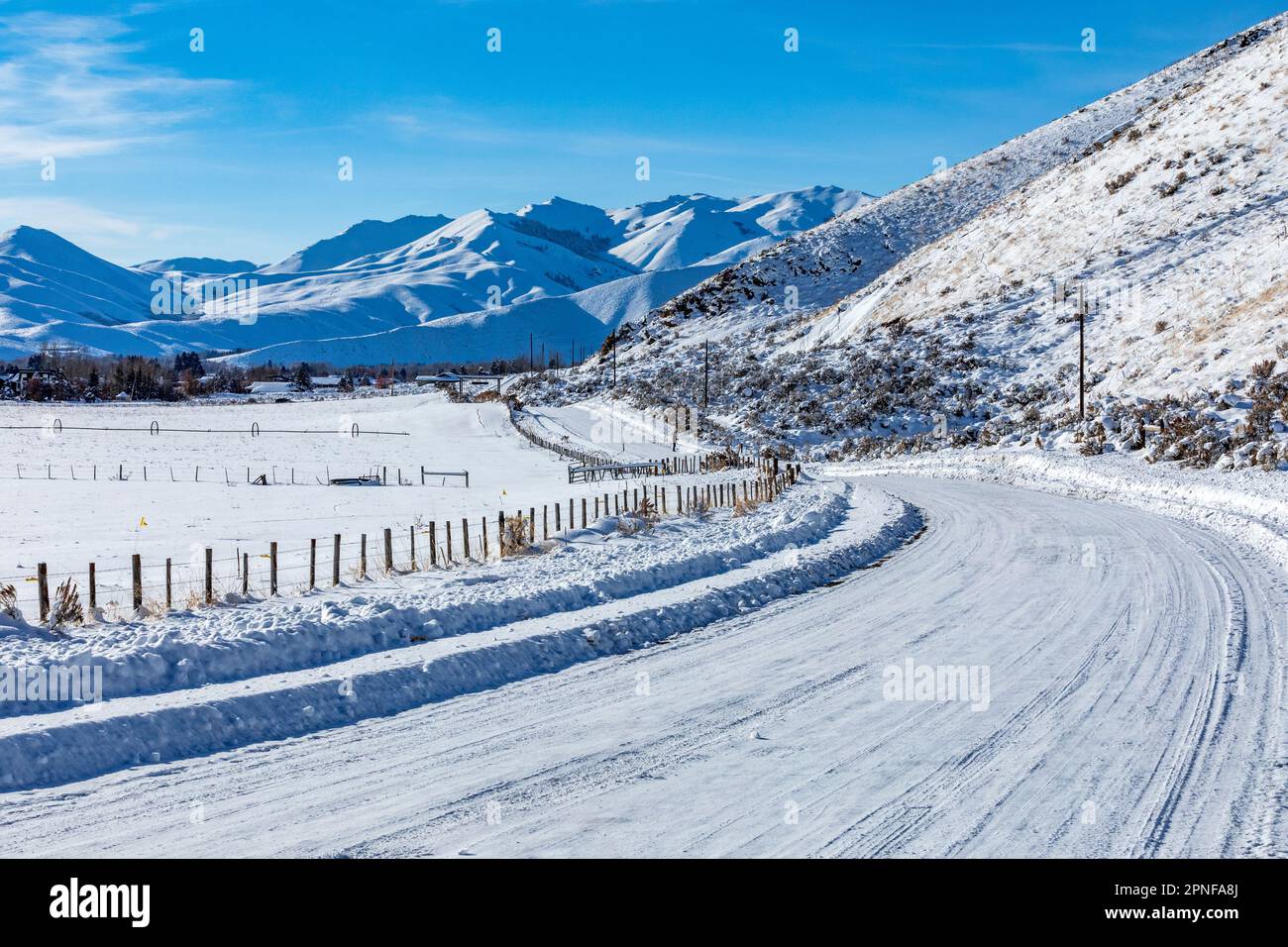 Stati Uniti, Idaho, Bellevue, neve coperta strada rurale con montagne in lontananza Foto Stock