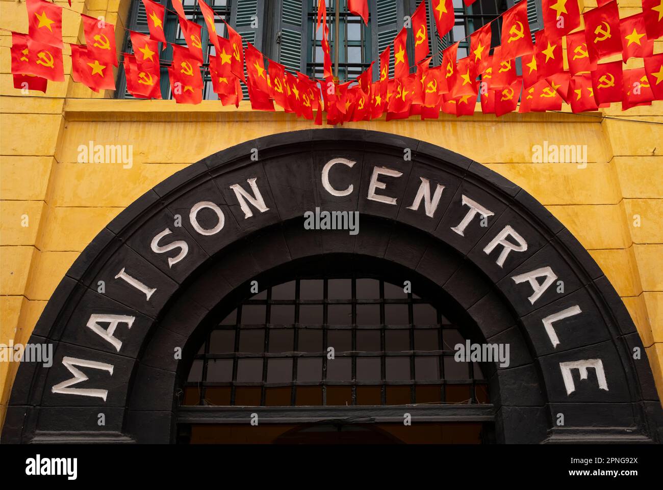 Vietnam: Le bandiere volano sopra l'ingresso al Museo della prigione di Hoa lo (la vecchia Maison Centrale francese), Hanoi. L'amministrazione coloniale francese costruì la prigione di Hoa lo nel 1896. Originariamente destinato a tenere 450 prigionieri, negli anni '1930s il numero dei detenuti era salito a quasi 2.000, la grande maggioranza dei prigionieri politici. La prigione di Hoa lo ha ottenuto notorietà durante la seconda Guerra di Indochina come luogo di incarcerazione per i piloti americani abbattuti, che ironicamente soprannominato la prigione “Hanoi Hilton”. Foto Stock