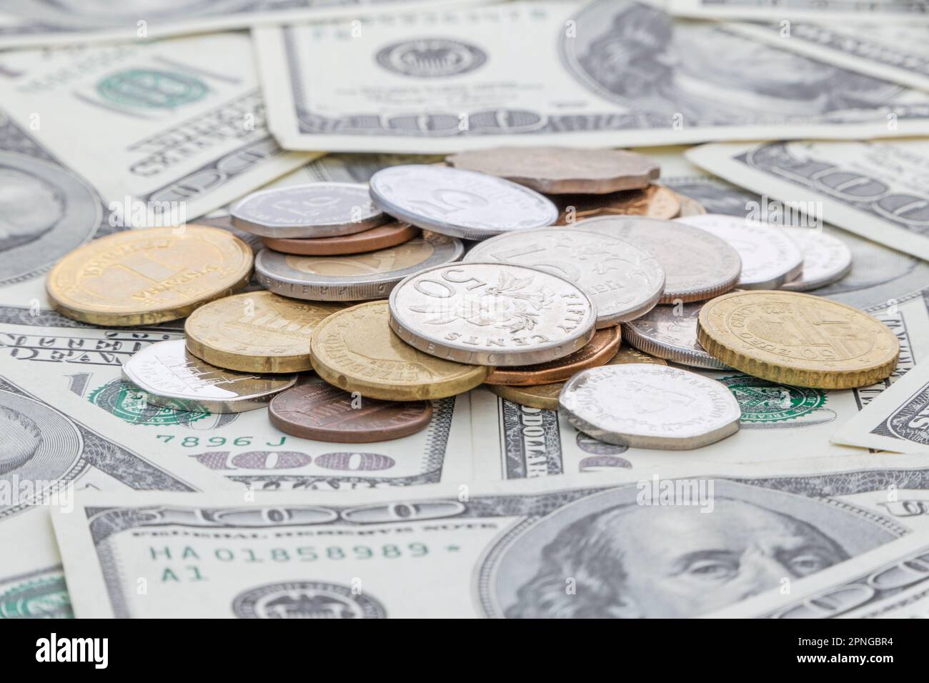 Cumulo di monete di paesi diversi giacenti su cento banconote in dollari USA Foto Stock