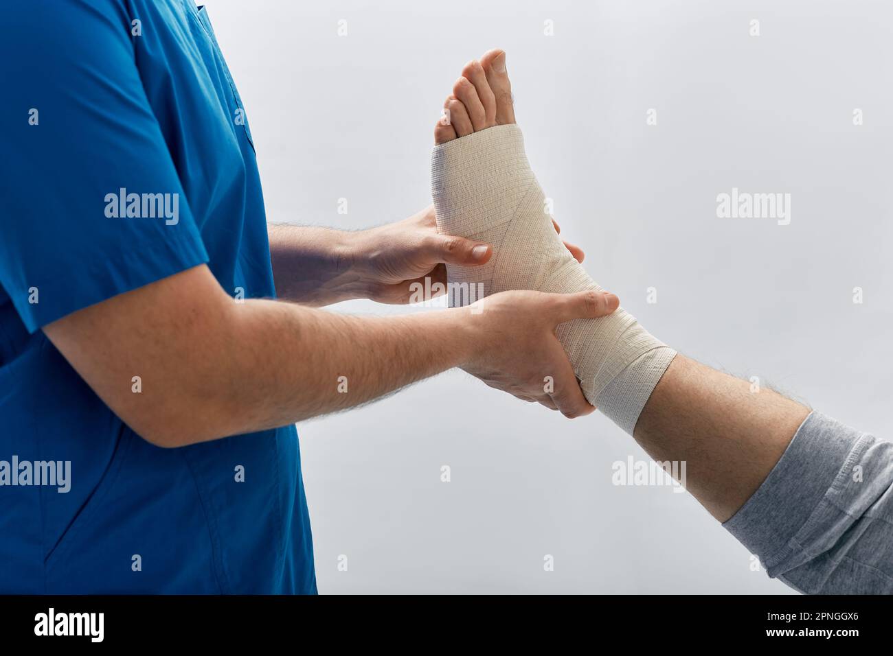 medico che avvolge il piede del paziente maschile con bendaggio elastico per trattare gli spruzzi muscolari nello studio medico della clinica medica Foto Stock