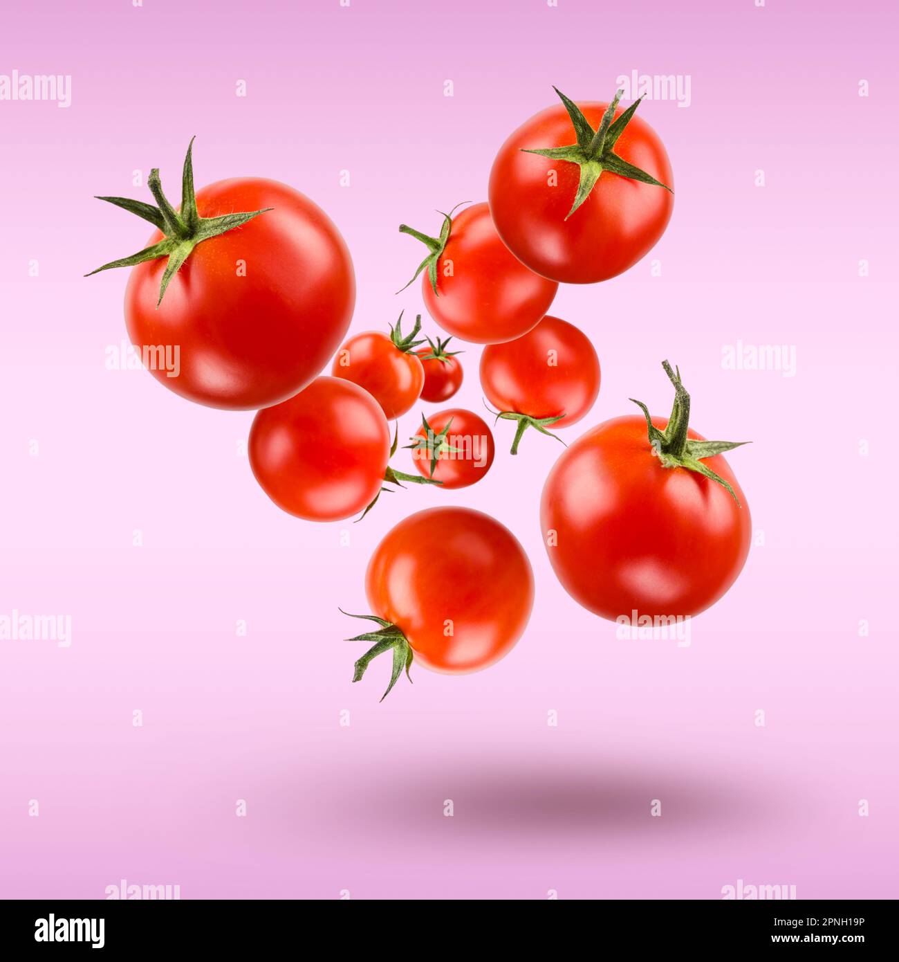 Piccoli pomodori ciliegini rossi galleggianti su sfondo viola. Foto Stock