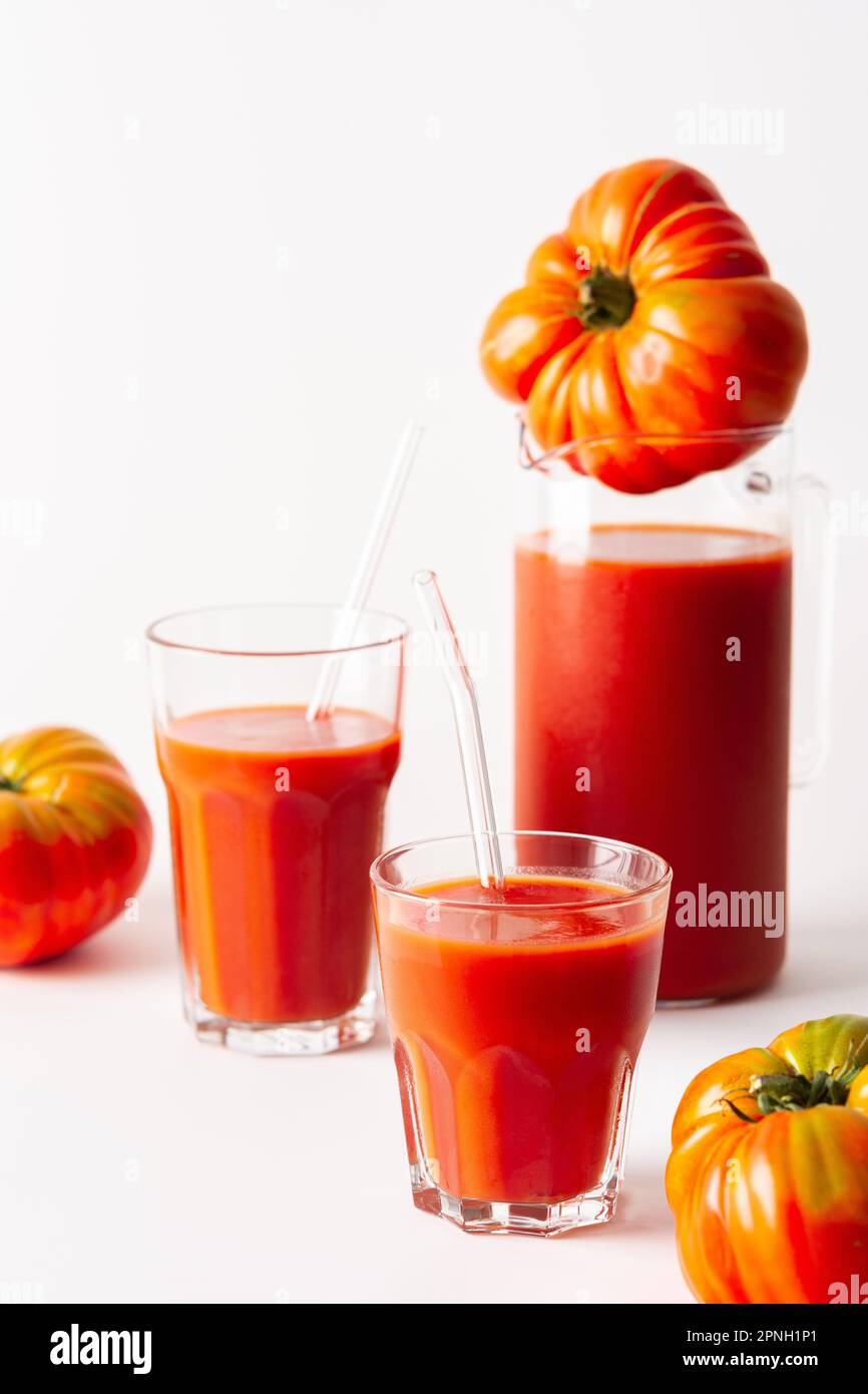 Succo di pomodoro appena spremuto in bicchieri e una caraffa con pomodori su sfondo bianco Foto Stock