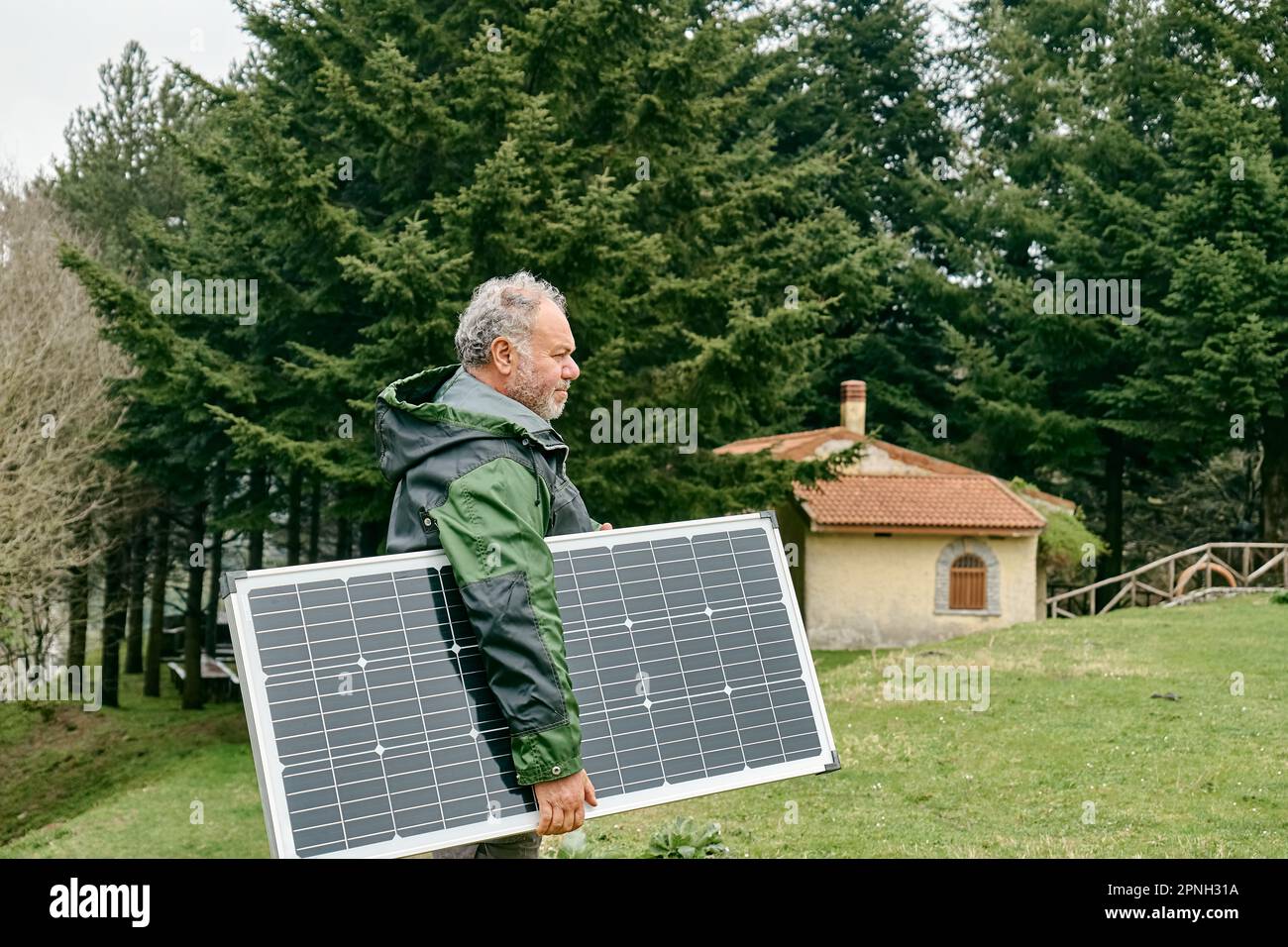 Uomo bearded di mezza età che trasporta il pannello solare vicino alla casa nella zona rurale. Energia alternativa, fonti di energia rinnovabile e risorse energetiche sostenibili co Foto Stock