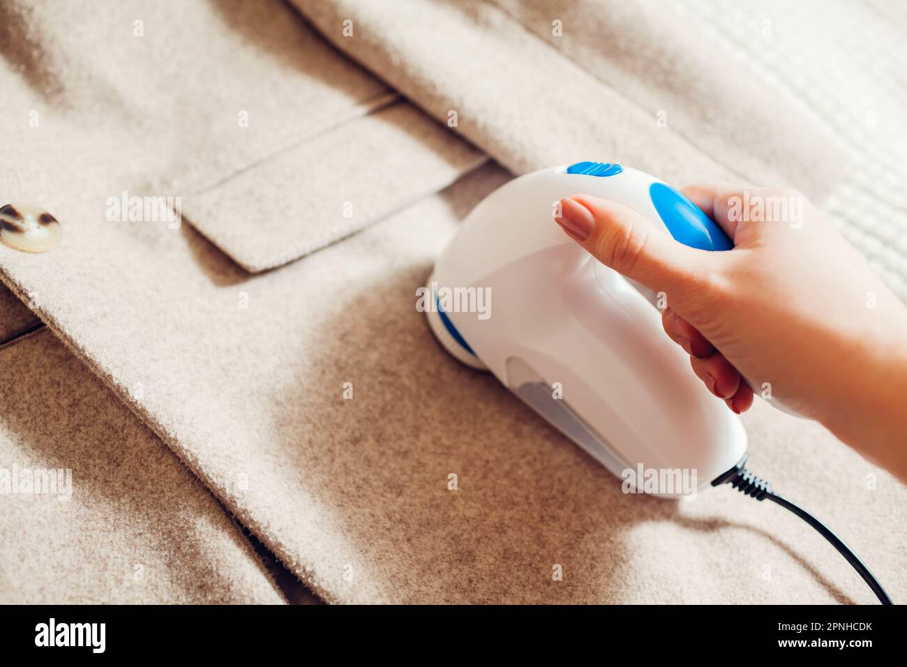 Donna che rimuove il pelucchi dai vestiti usando il rasoio fuzz a casa. Primo piano di un dispositivo elettrico portatile cablato. Cura degli indumenti. Macchina per la casa Foto Stock