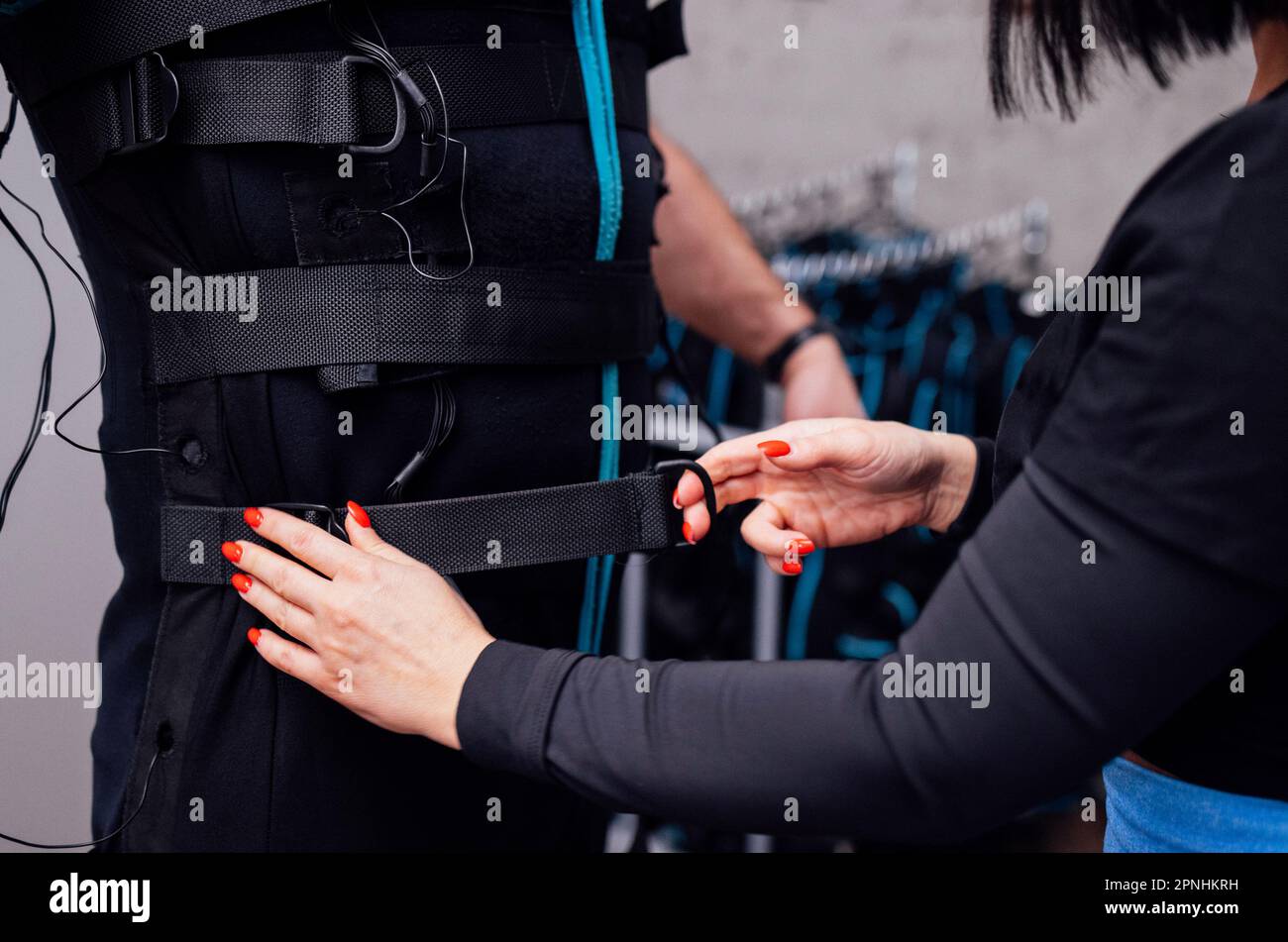 L'istruttore femmina fissa le attrezzature necessarie su ems Suit al cliente maschio. Il coach di idoneità mette sul costume per l'allenamento elettrico di stimolazione del muscolo sul anziano Foto Stock