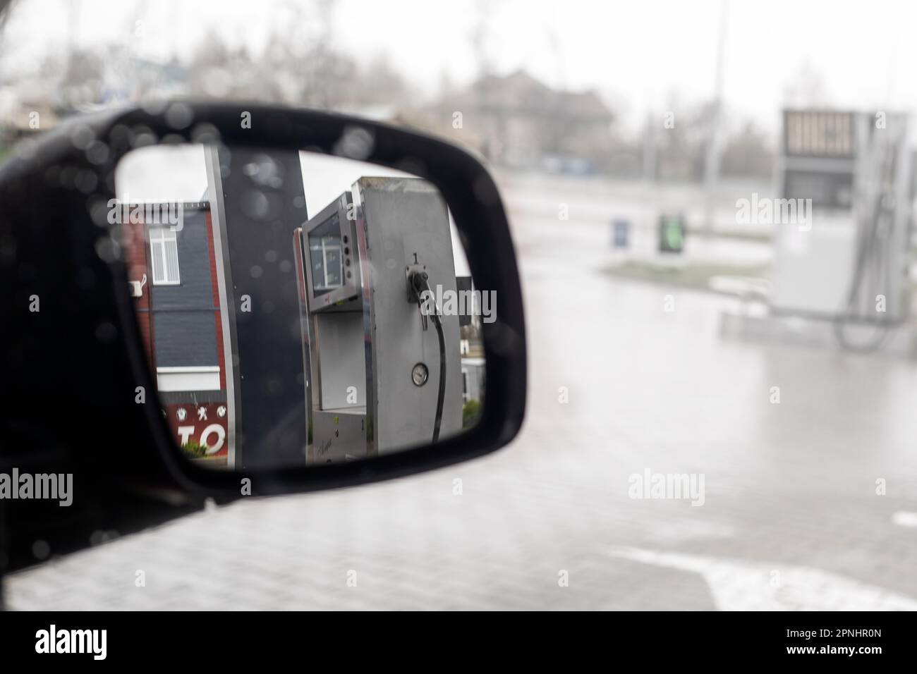 vedere la stazione di servizio nello specchietto destro della vettura sul lato conducente sotto la pioggia.orizzontale Foto Stock