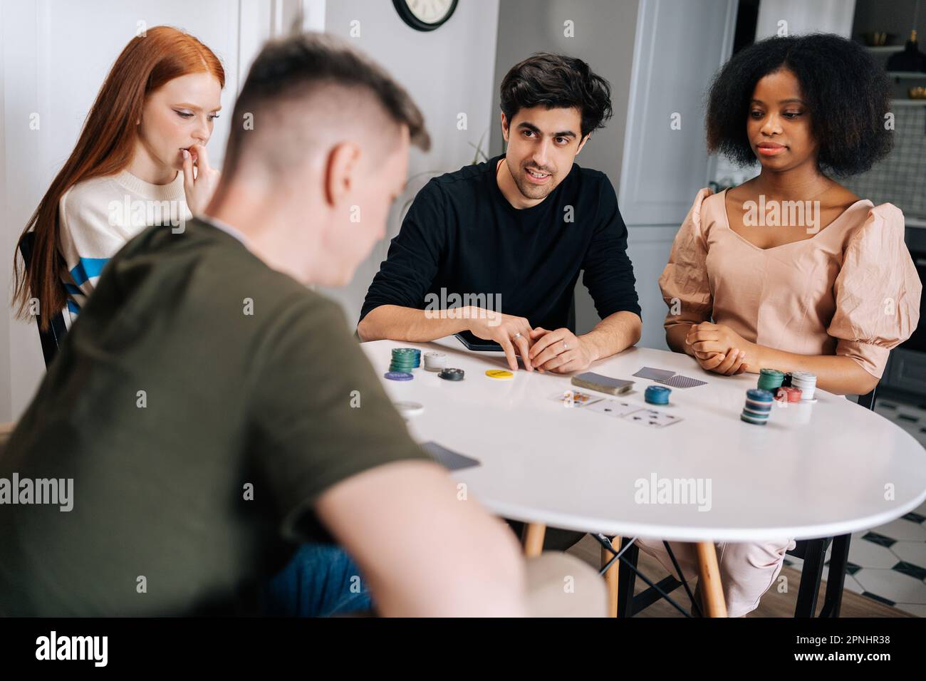 Gruppo di giovani amici multietnici che hanno festa a casa durante i fine settimana giocando a poker gioco di carte in soggiorno e parlando. Foto Stock
