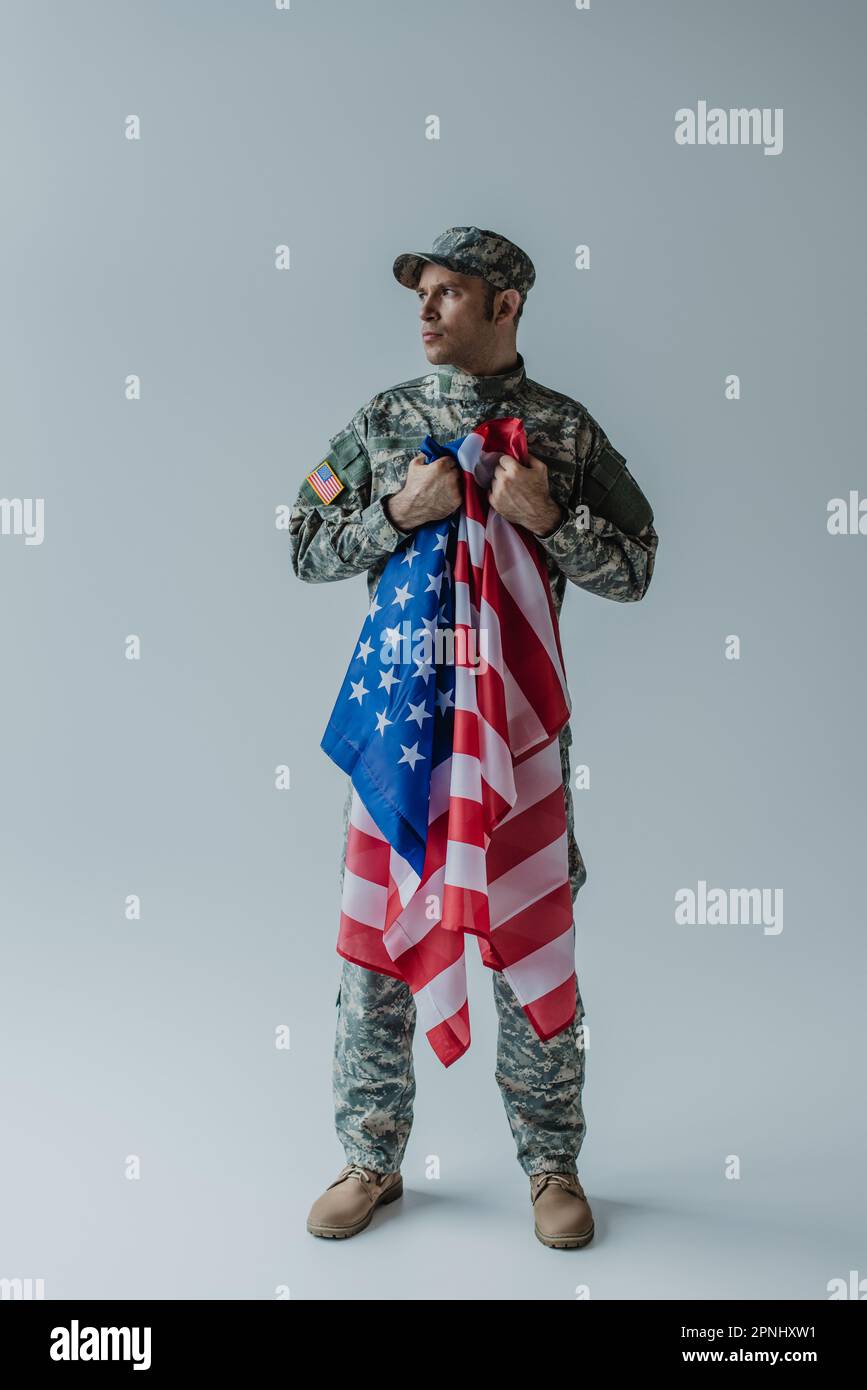 Tutta la lunghezza del soldato americano che detiene la bandiera degli Stati Uniti durante la giornata commemorativa in grigio Foto Stock