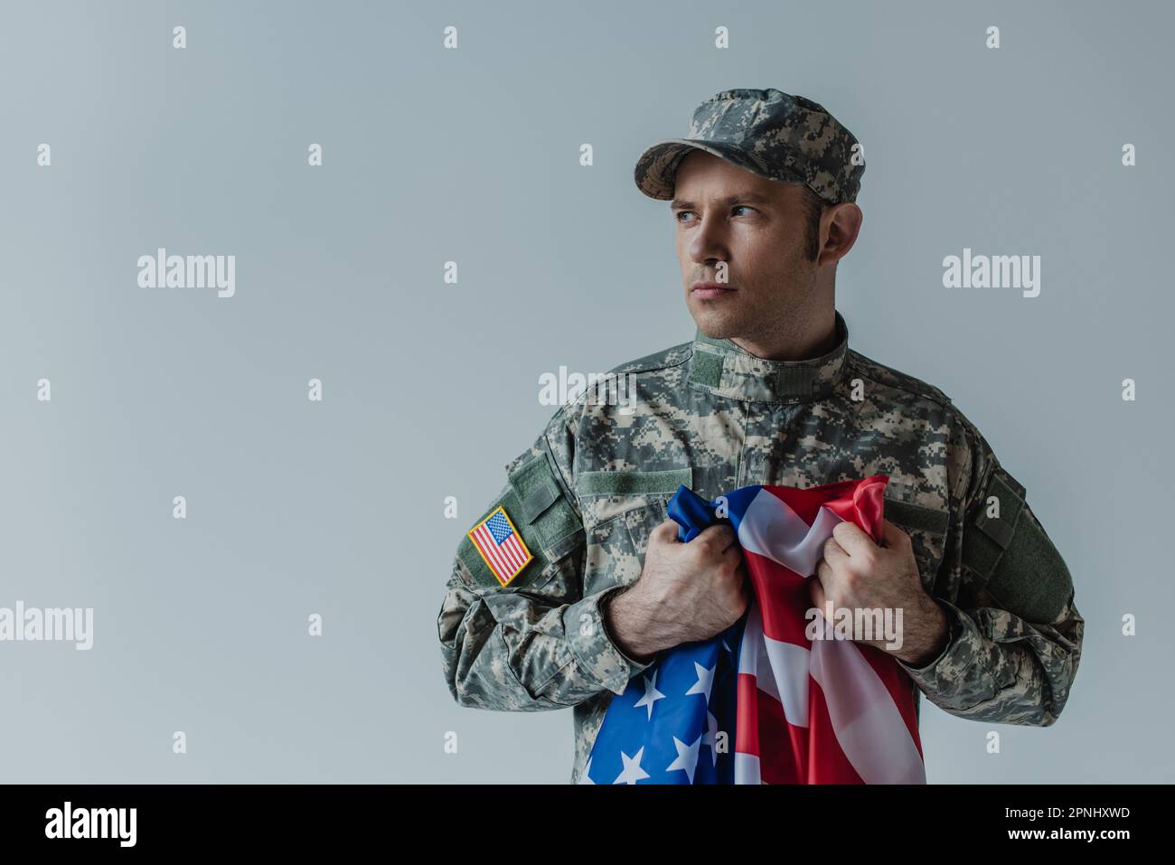 Soldato americano che detiene la bandiera degli Stati Uniti mentre piangono durante il Memorial Day isolato sul grigio Foto Stock