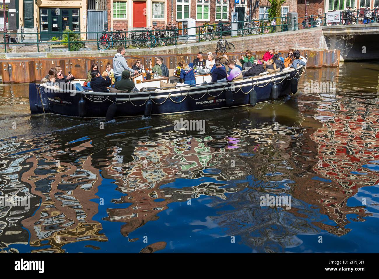 Friendship Luxury Canal Cruises tour in barca lungo il canale con riflessi colorati in acqua ad Amsterdam, Olanda, Paesi Bassi nel mese di aprile Foto Stock