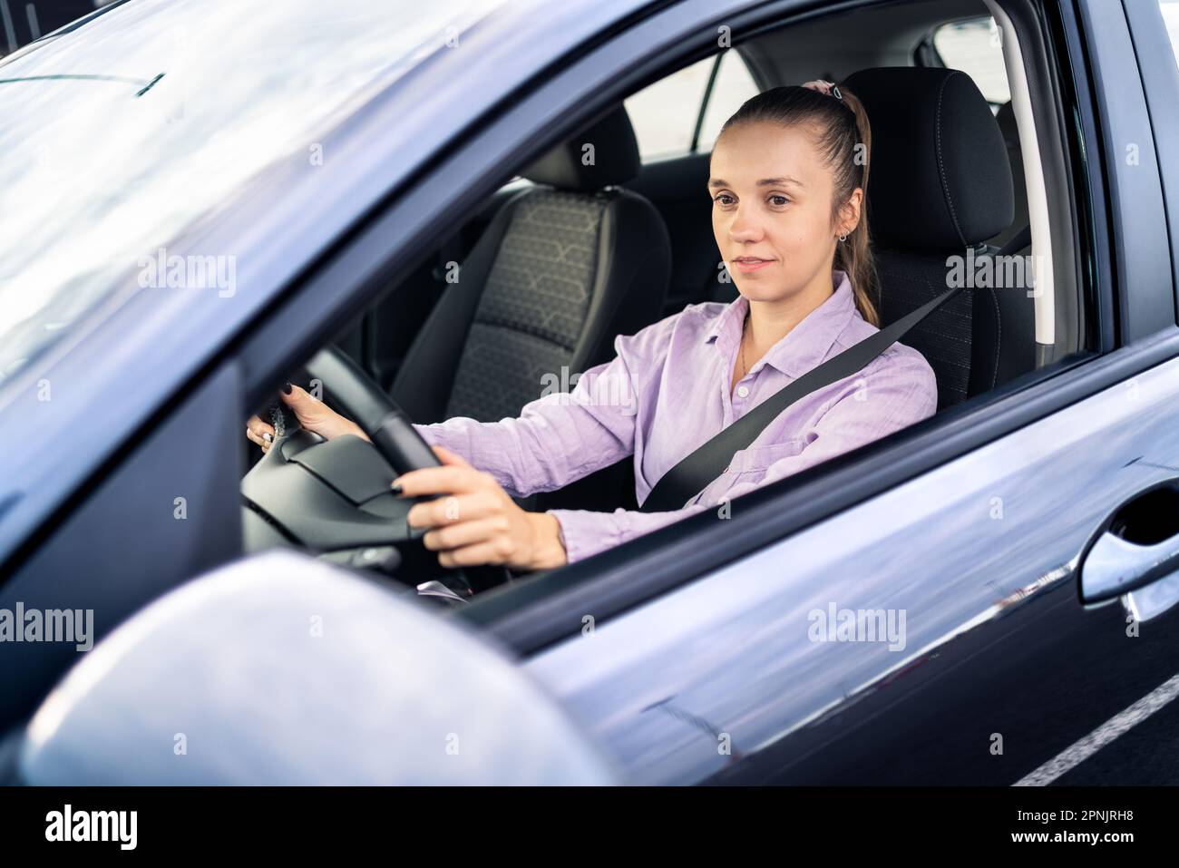 Auto alla guida. Donna felice. Tassista femminile. Noleggio o vendita di veicoli, concessionaria, autista o servizio di rideshare. Cintura di sicurezza accesa. Foto Stock