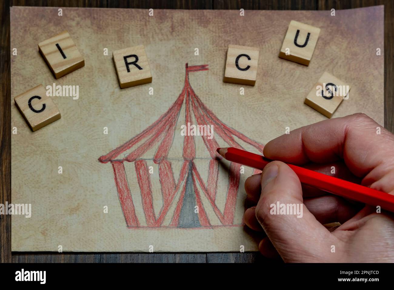 Una mano maschio sta colorando un disegno che rappresenta una tenda da circo con una matita rossa Foto Stock