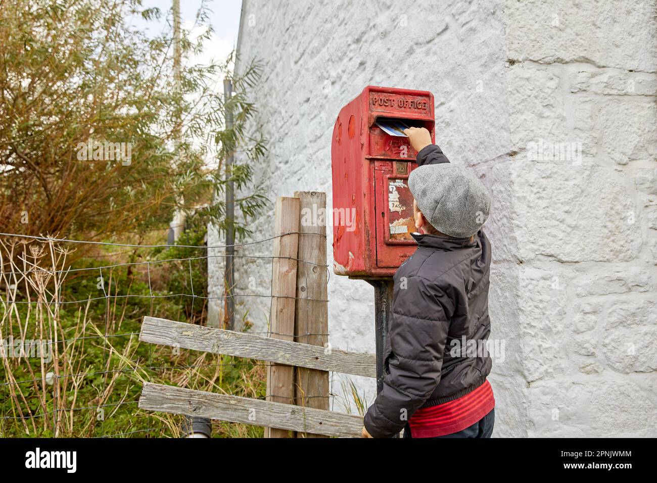 Young Boy a Skye Weavers Cap Mailing cartolina alla Royal mailbox Stein, Isola di Skye, Scozia, Regno Unito Foto Stock