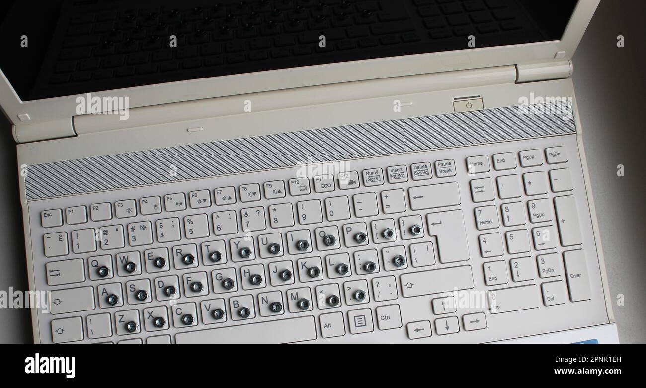 Vista dall'alto del computer portatile con dadi in ferro sovrappone lettere russe ai tasti della tastiera Foto Stock