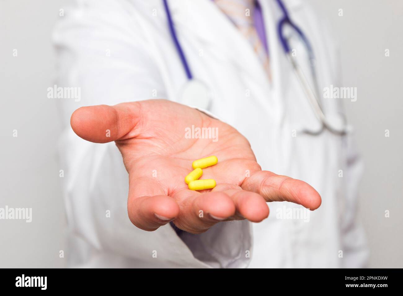 Primo piano di una mano di un medico caucasico irriconoscibile che tiene tre pillole gialle. Foto Stock